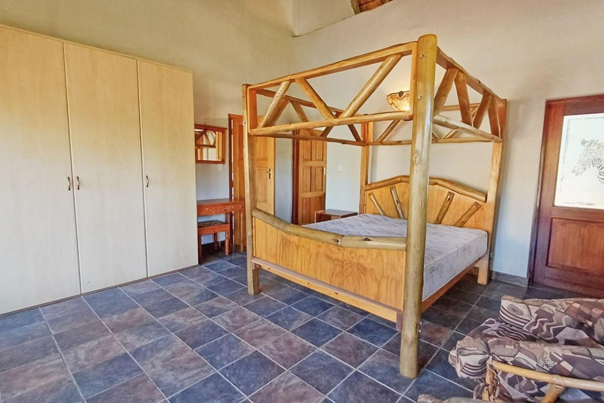 A spacious bedroom featuring tiled flooring, built-in cupboards, and a vaulted ceiling, offering a rustic aesthetic with natural wood elements.