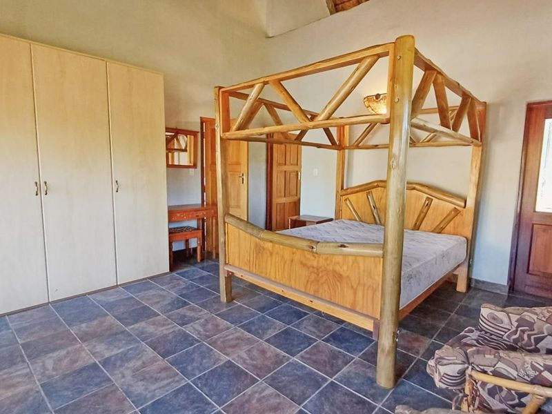 A spacious bedroom featuring tiled flooring, built-in cupboards, and a vaulted ceiling, offering a rustic aesthetic with natural wood elements.