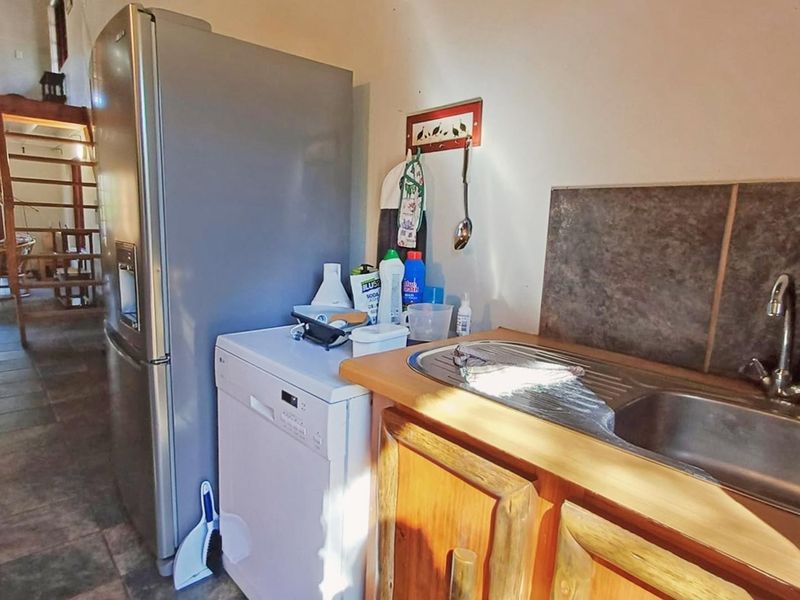 A functional kitchen area featuring wooden cabinetry, a stainless steel sink, and tiled flooring, with an open-plan layout leading to a staircase.