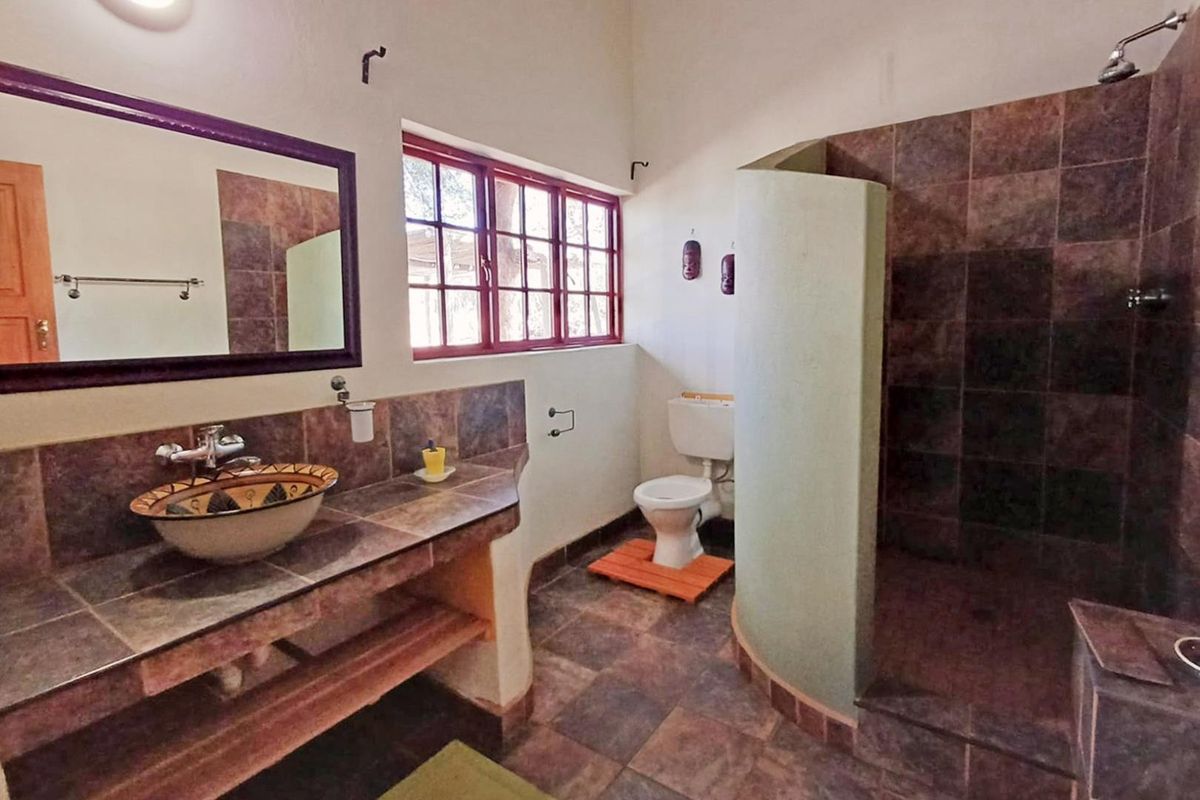 A bathroom featuring a tiled vanity with a vessel sink, a walk-in shower with dark tiling, and a toilet.