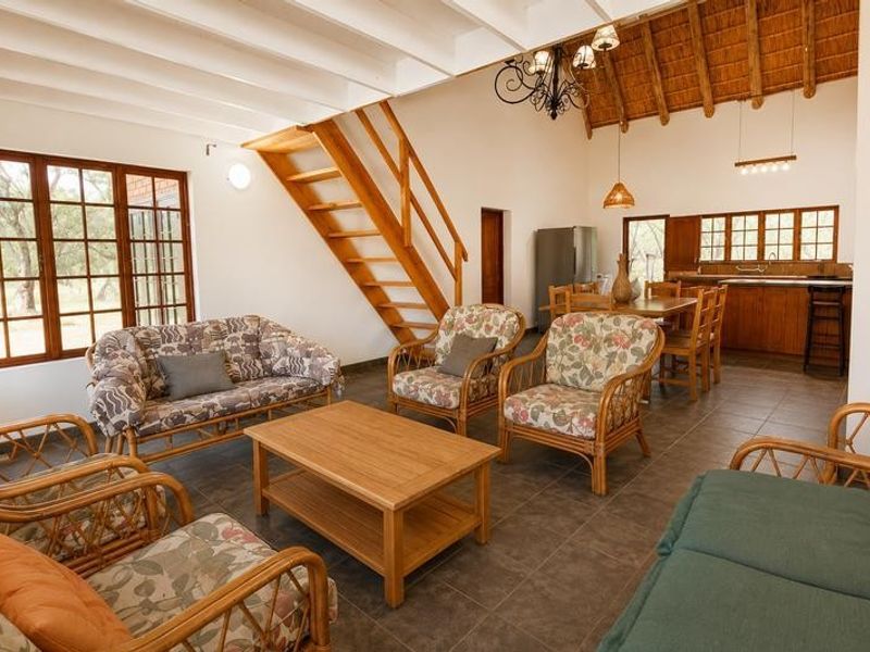 Spacious open-plan living and dining area featuring exposed beam ceilings, a wooden staircase, and an integrated kitchen with tiled flooring throughout.