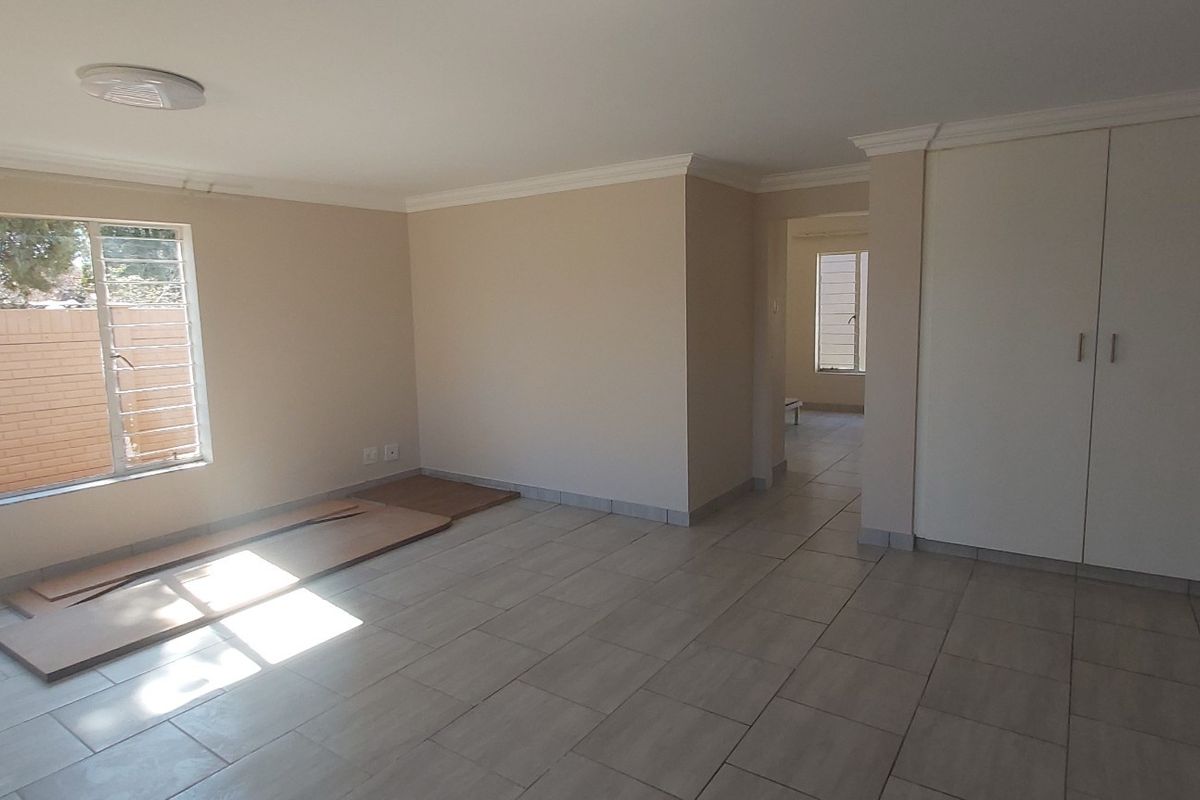 A bright, empty living room featuring neutral tiled flooring, built-in storage cupboards, and large windows allowing for ample natural light.