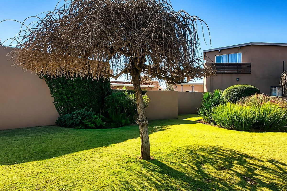 A well-maintained rear garden featuring a manicured lawn, established landscaping, and a boundary wall, with a view of the property's rear elevation.