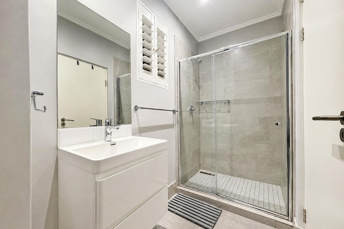 Modern bathroom featuring a sleek vanity, large wall mirror, and a spacious walk-in shower with glass sliding doors and neutral tiling.