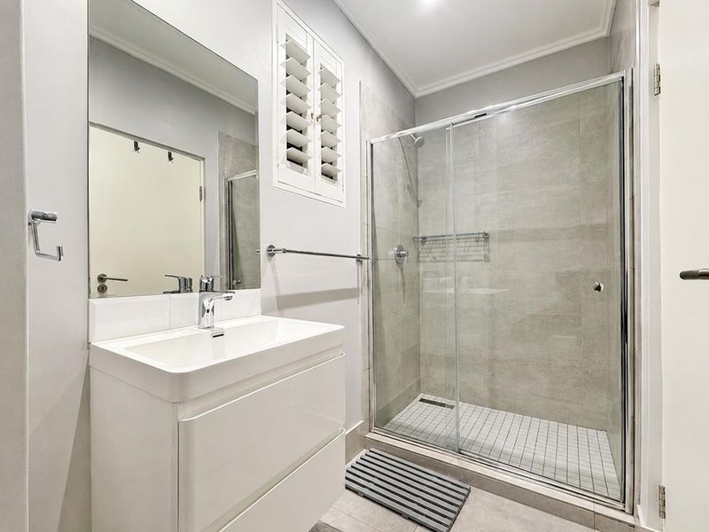 Modern bathroom featuring a sleek vanity, large wall mirror, and a spacious walk-in shower with glass sliding doors and neutral tiling.
