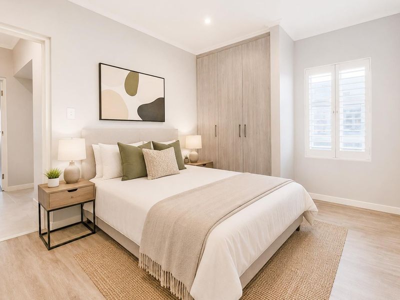A well-maintained bedroom featuring light wood-look flooring, built-in cabinetry, and plantation shutters, offering a bright and neutral living space.