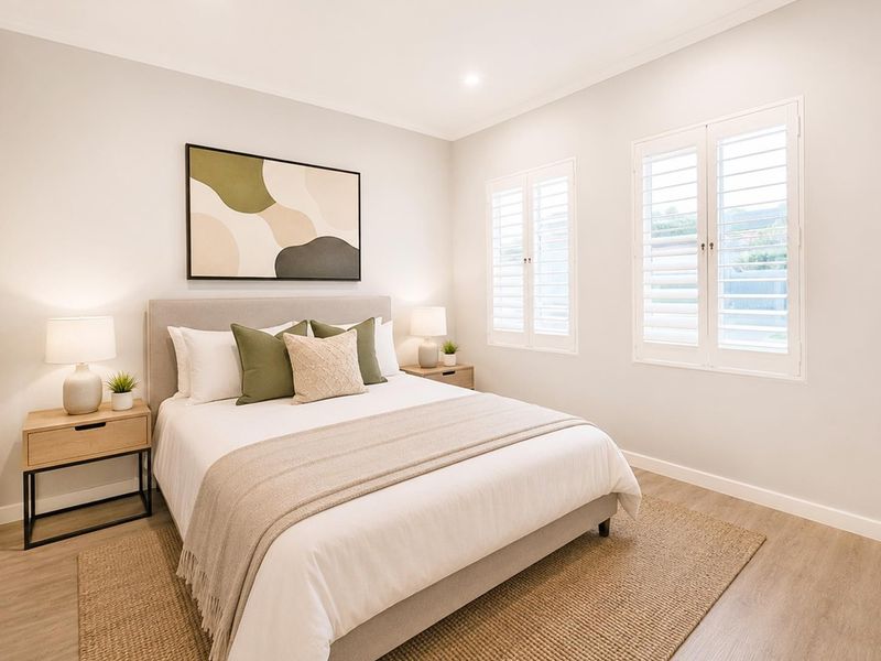 A well-presented bedroom featuring neutral tones, plantation shutters, built-in wardrobe storage, and modern recessed lighting.