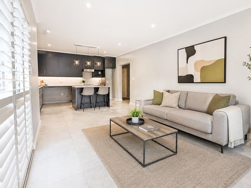 Modern open-plan living area featuring a sleek kitchen with dark cabinetry, a central island, and neutral tiled flooring throughout.