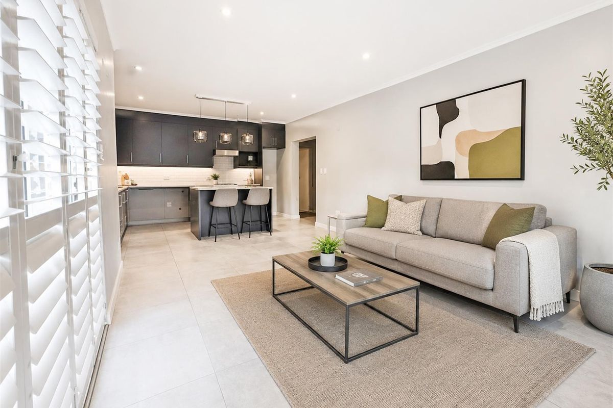 Modern open-plan living area featuring a sleek kitchen with dark cabinetry, a central island, and neutral tiled flooring throughout.