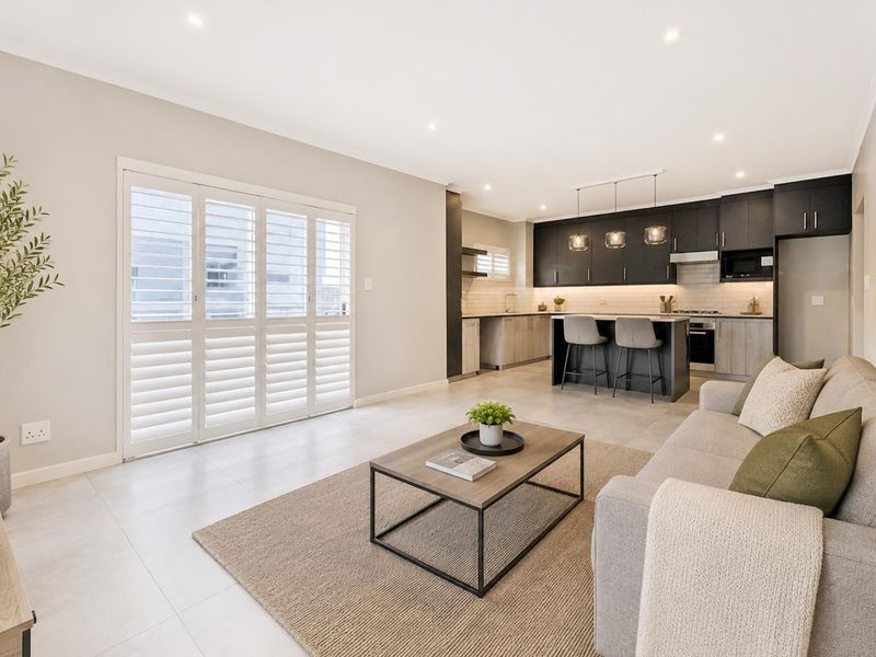 Modern open-plan living area featuring a sleek kitchen with island, built-in appliances, tiled floors, and shutter doors leading to outdoor space.