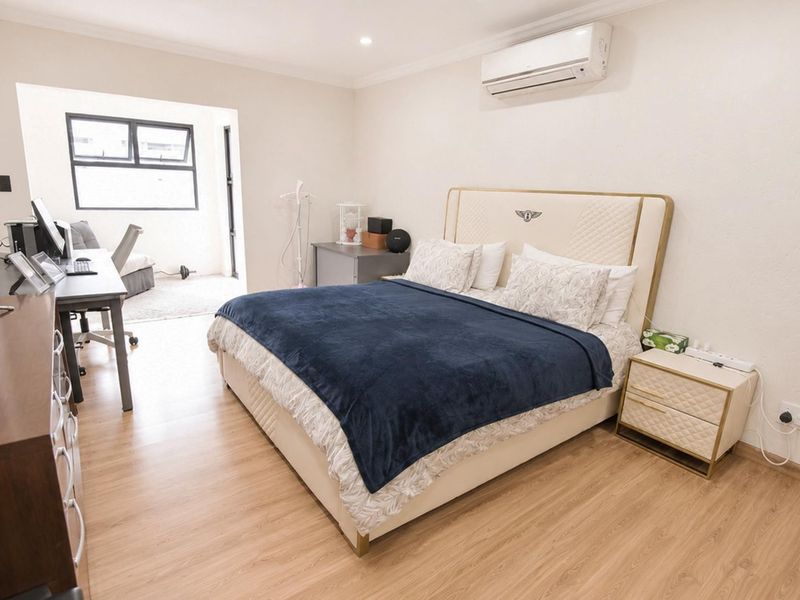 Spacious bedroom featuring laminate flooring, split-system air conditioning, and an adjoining study or sunroom area with large windows.