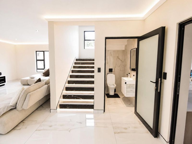 Modern open-plan living area featuring polished marble-look flooring, a contemporary staircase with integrated lighting, and an adjacent guest bathroom with high-end finishes.