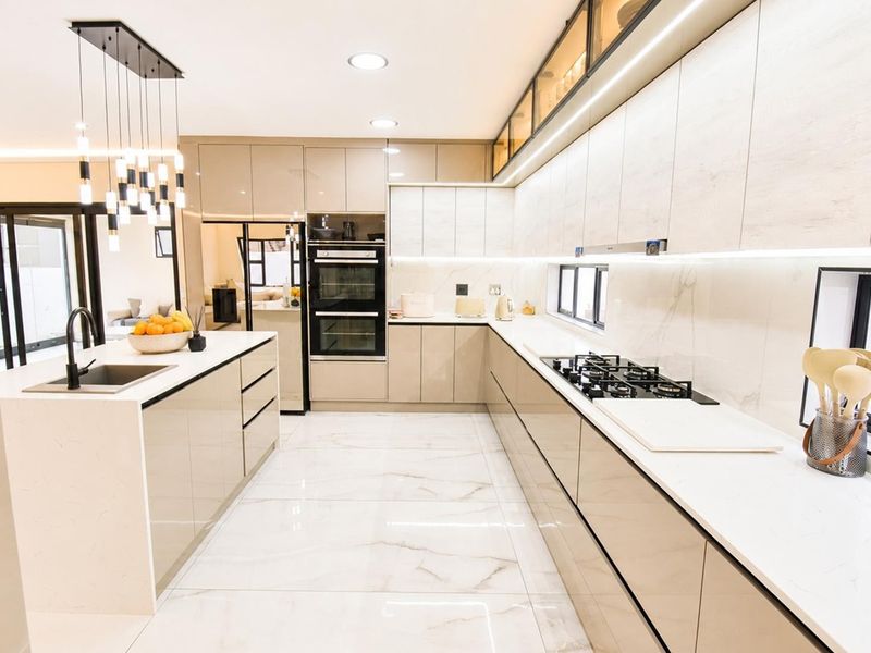 Modern, high-end kitchen featuring sleek integrated cabinetry, a central island with an undermount sink, built-in double oven, gas hob, and elegant marble-look flooring.