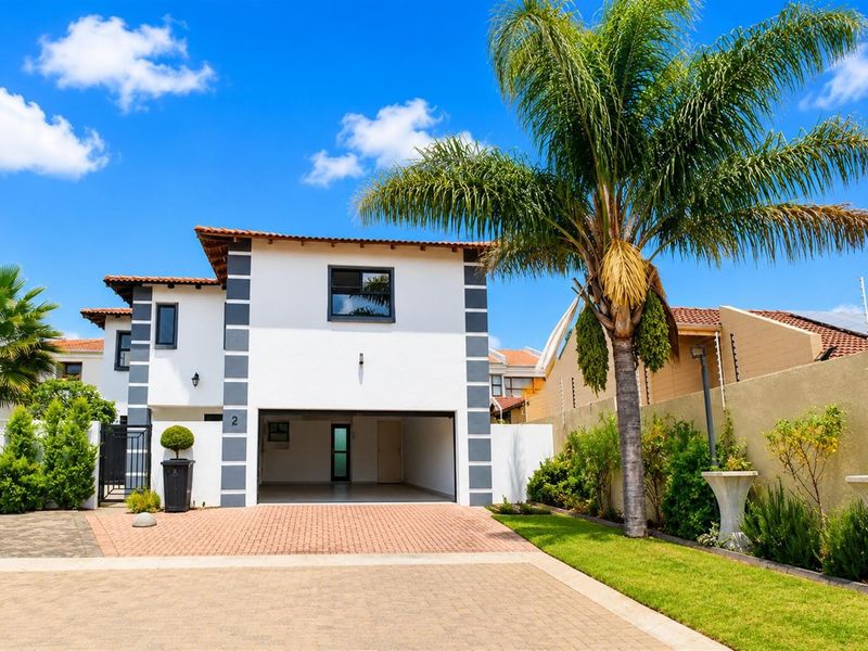 Front elevation of a modern two-story house featuring a paved driveway, double garage, and well-maintained garden with electric perimeter fencing.