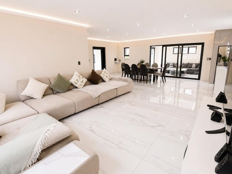 Spacious open-plan living and dining area featuring large format marble-look floor tiles, recessed downlighting, and seamless access to the outdoor patio through sliding glass doors.