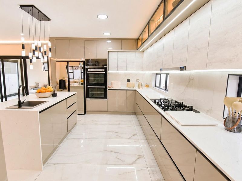 Modern, high-end kitchen featuring sleek cabinetry, quartz countertops, a central island, built-in appliances, and elegant marble-look flooring with integrated lighting.