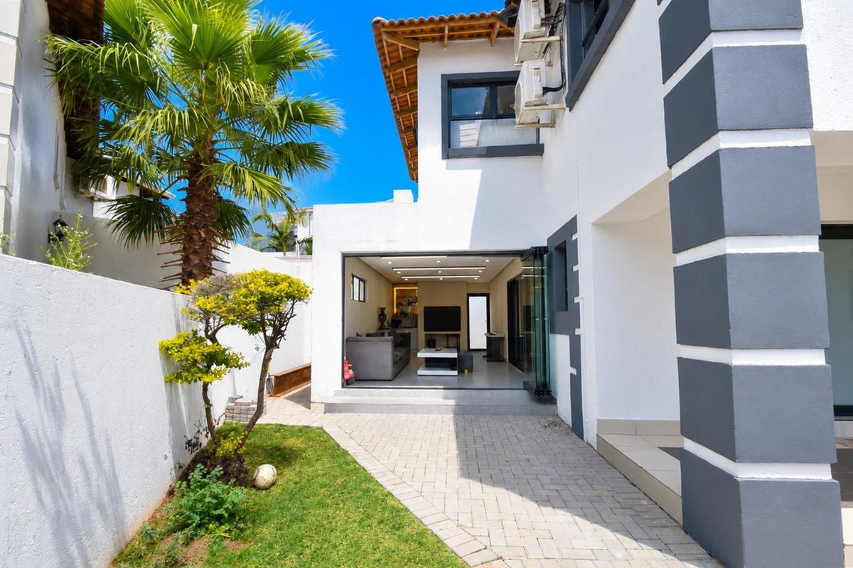 Rear view of the property featuring a paved patio area, landscaped garden, and bi-fold doors leading into the open-plan living space.