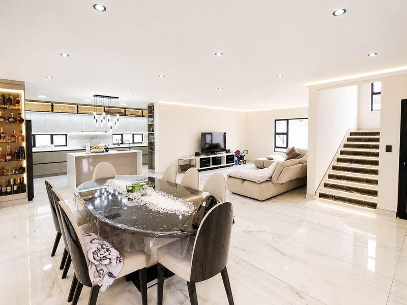 Spacious open-plan living, dining, and kitchen area featuring high-end marble-look flooring, modern cabinetry, and a striking illuminated staircase.