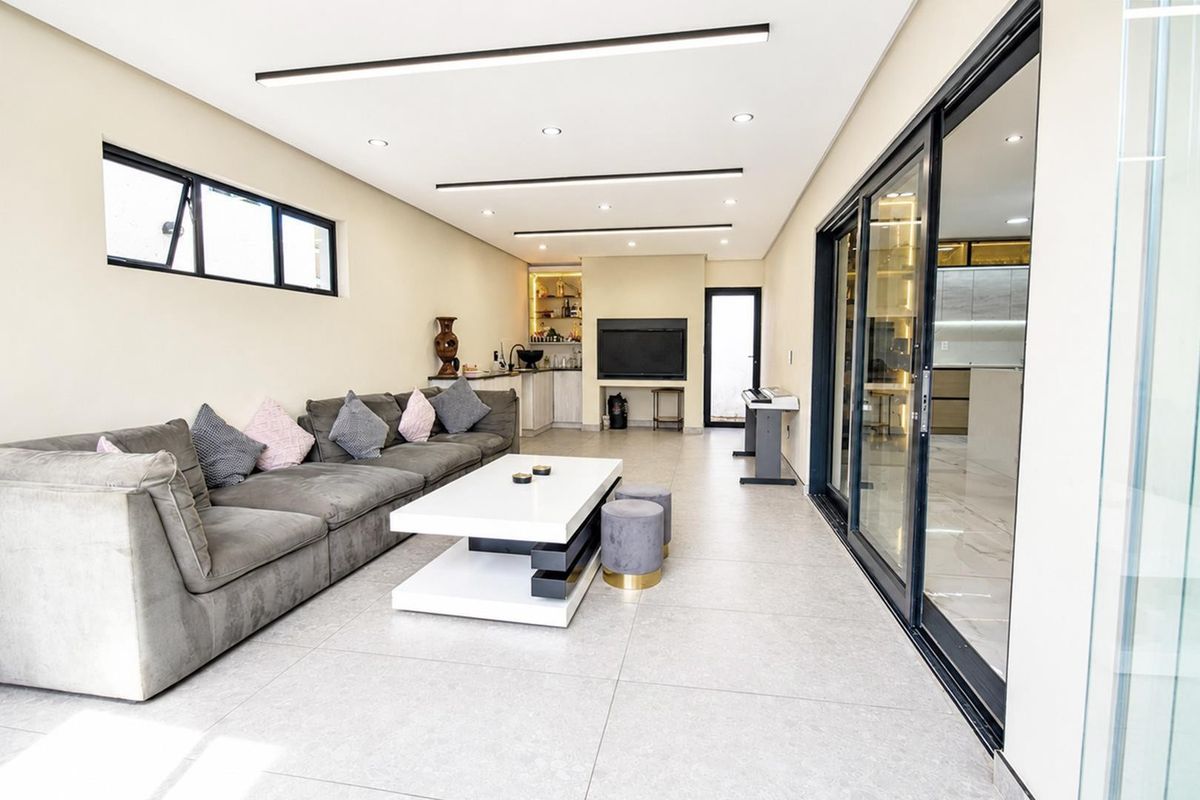 Modern living room featuring large format floor tiles, recessed linear lighting, and sliding glass doors that provide seamless access to the adjacent kitchen area.