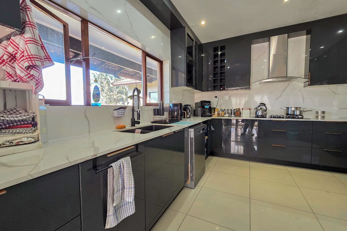 Modern kitchen featuring high-gloss dark cabinetry, stone countertops, marble-look backsplash, and integrated appliances with recessed lighting and large format floor tiles.