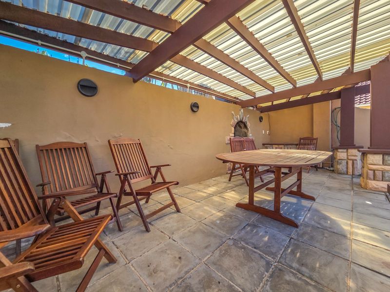 Covered outdoor patio area featuring a timber pergola, translucent roof, and stone paved flooring, suitable for alfresco dining and entertainment.