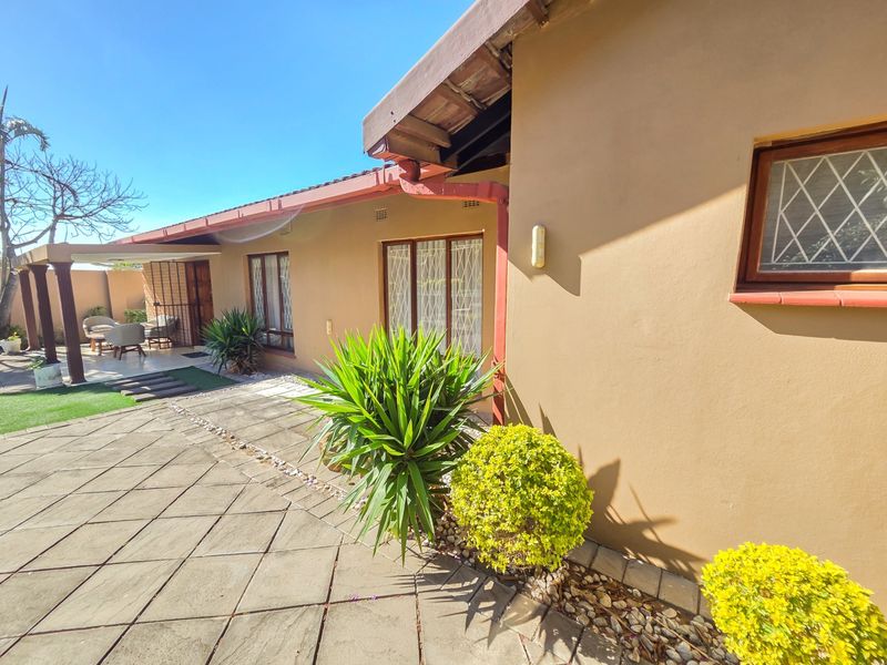 A rear exterior view of the house featuring a paved patio area, tiled roof, and diamond-pattern security bars on the windows.