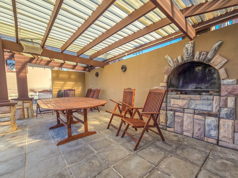 Covered outdoor patio featuring a timber pergola, stone-clad built-in braai, and stone paving, ideal for alfresco dining and entertaining.