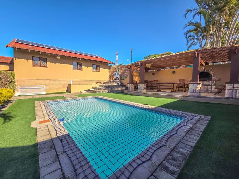 Outdoor entertainment area featuring a swimming pool, artificial lawn, and a covered pergola with a built-in braai, ideal for relaxed outdoor living.
