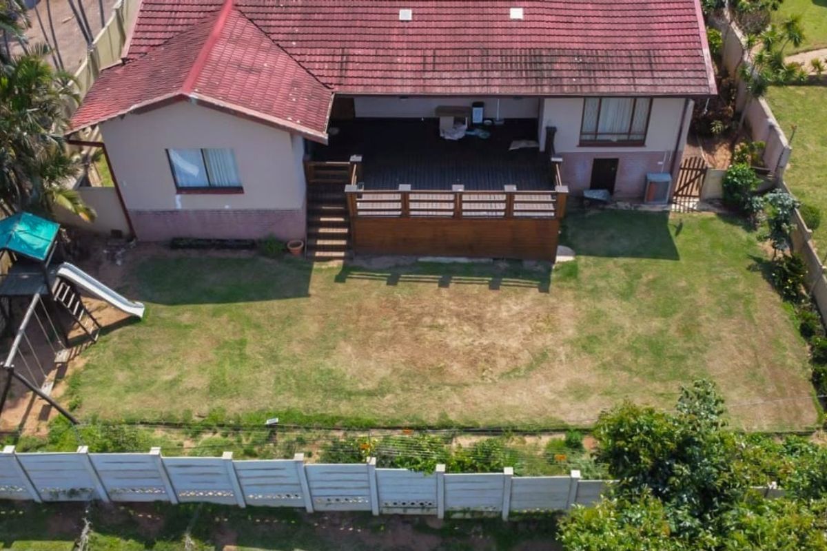 Aerial view of the property featuring a rear timber deck, tiled roof, and a spacious backyard enclosed by a precast concrete boundary wall.