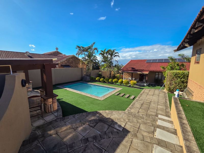 A well-maintained outdoor entertainment area featuring a swimming pool, artificial lawn, paved patio, and a pergola, set within a private garden.