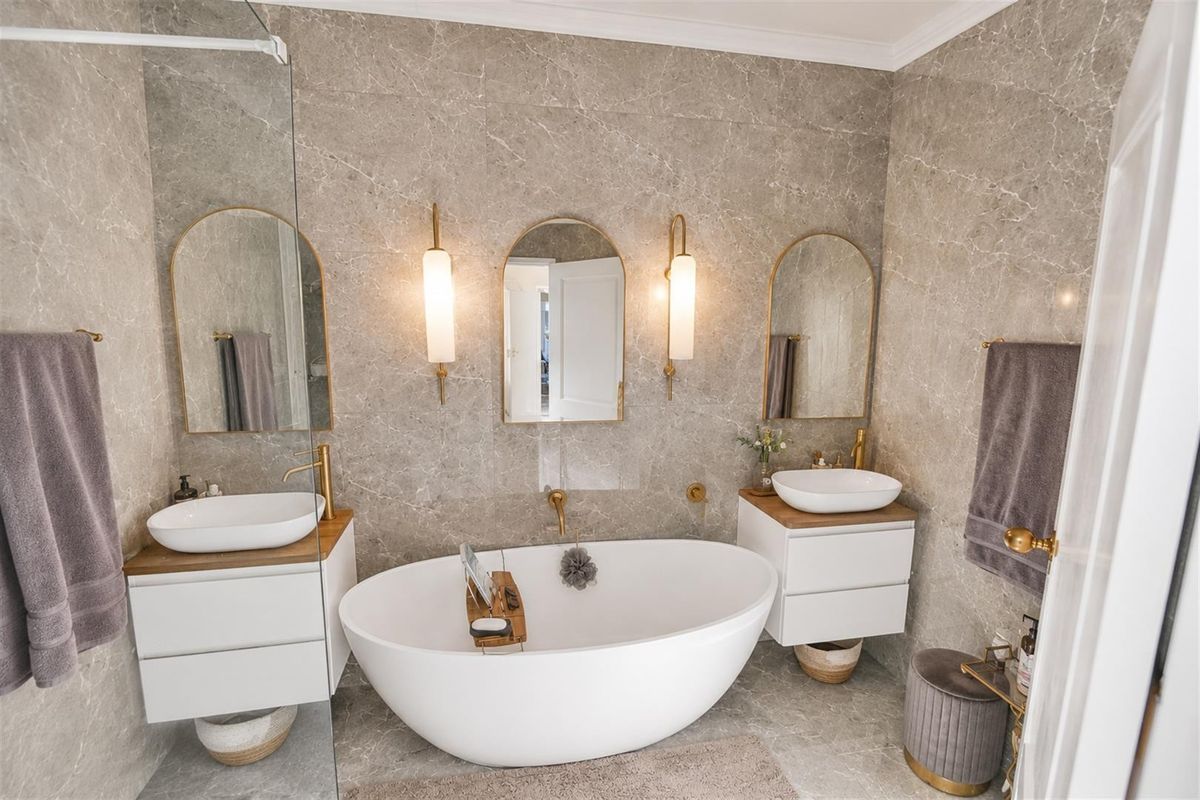 Modern luxury bathroom featuring a freestanding bathtub, dual vanity with vessel sinks, elegant wall sconces, and premium stone wall and floor tiling.