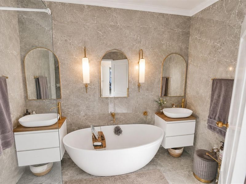 Modern luxury bathroom featuring a freestanding bathtub, dual vanity with vessel sinks, elegant wall sconces, and premium stone wall and floor tiling.