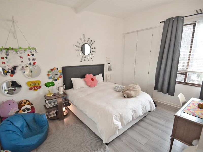 A well-lit bedroom featuring laminate flooring, a built-in wardrobe, and a window with a curtain rod, offering a functional and comfortable living space.