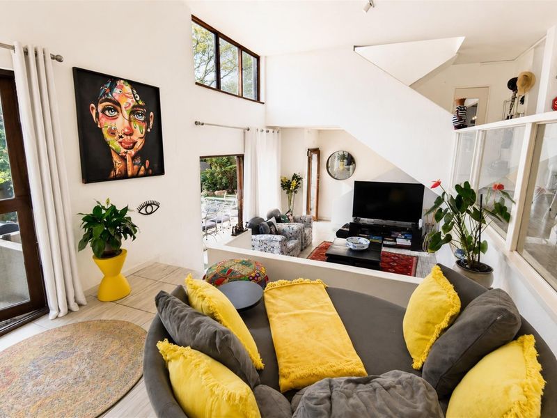 Spacious open-plan living area featuring double volume ceilings, a modern staircase with glass balustrade, and large sliding doors leading to the garden.