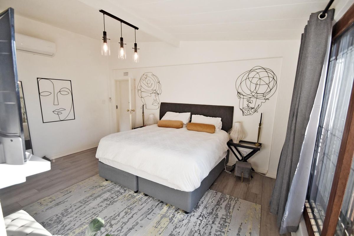 A well-maintained bedroom featuring timber-look laminate flooring, an exposed beam ceiling, and a split-system air conditioner, with access to an outdoor area.