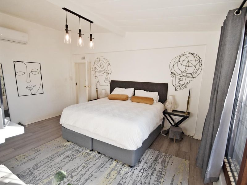 A well-maintained bedroom featuring timber-look laminate flooring, an exposed beam ceiling, and a split-system air conditioner, with access to an outdoor area.