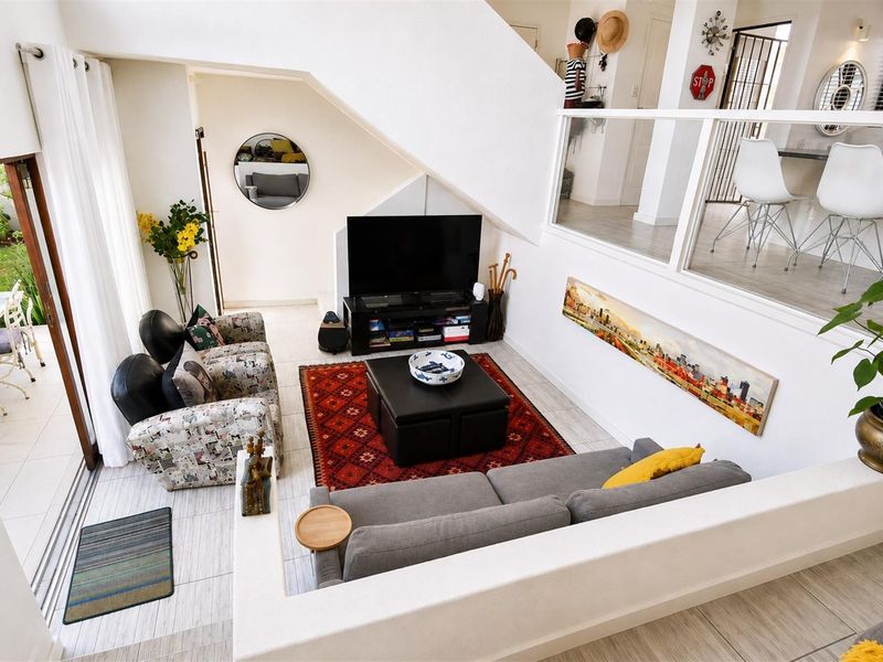A bright, open-plan living area featuring a staircase with a modern glass balustrade, tiled flooring, and large sliding doors leading to an outdoor patio.