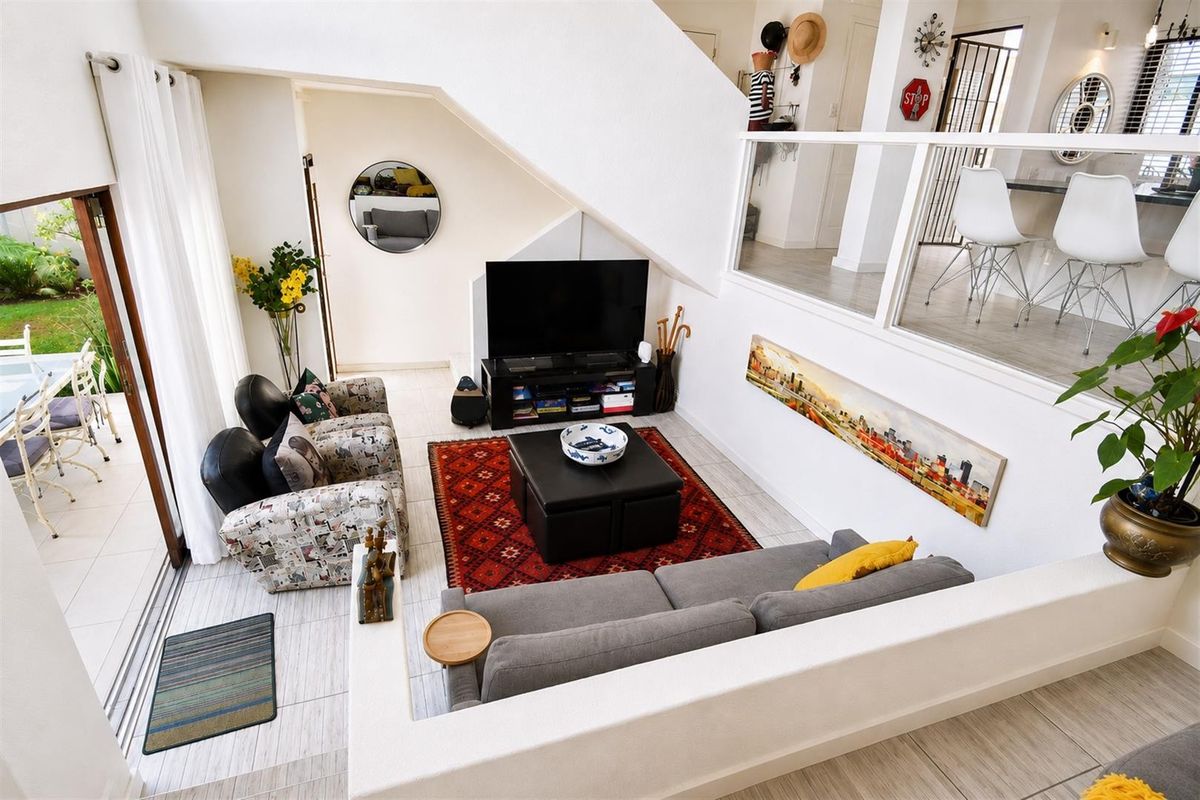 A bright, open-plan living area featuring a staircase with a modern glass balustrade, tiled flooring, and large sliding doors leading to an outdoor patio.