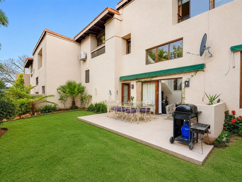 Rear view of the townhouse featuring a paved patio area, retractable awning, sliding door access, and a well-maintained private garden.
