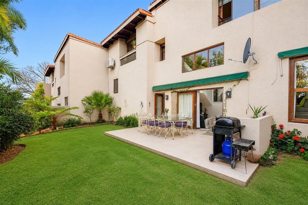 Rear view of the townhouse featuring a paved patio area, retractable awning, sliding door access, and a well-maintained private garden.