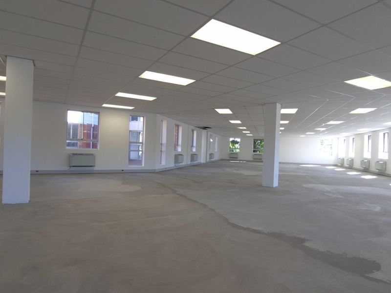 Expansive open-plan commercial space featuring a suspended ceiling, recessed lighting, structural columns, and large windows with integrated HVAC units.
