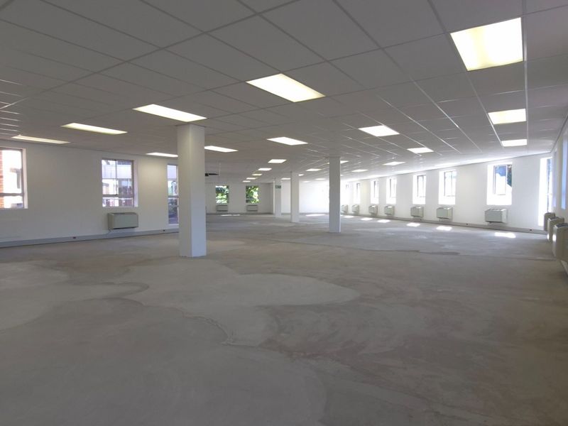 Expansive open-plan retail or office space featuring a suspended ceiling, recessed lighting, structural columns, and multiple wall-mounted air conditioning units.