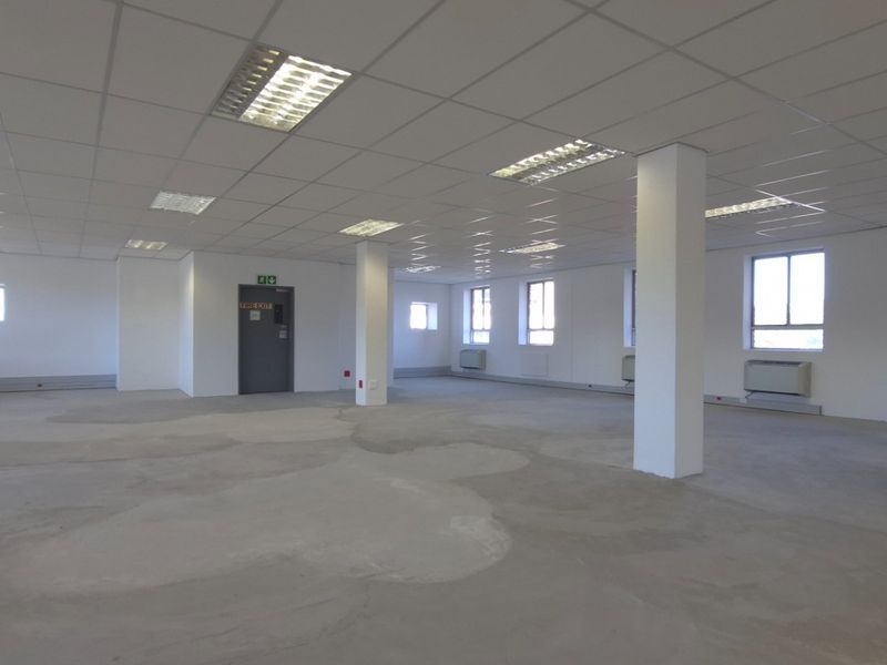 Spacious open-plan commercial office area featuring a suspended ceiling, recessed lighting, structural columns, and wall-mounted HVAC units, ready for custom flooring installation.