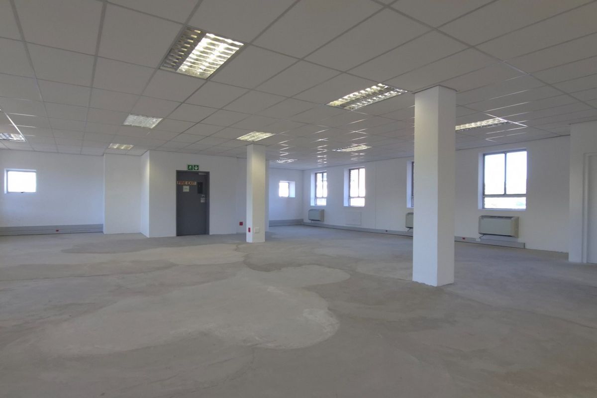 Spacious open-plan commercial office area featuring a suspended ceiling, recessed lighting, structural columns, and wall-mounted HVAC units, ready for custom flooring installation.