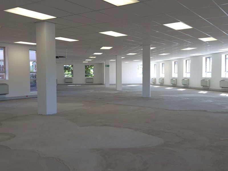 Spacious open-plan retail or office area featuring a suspended ceiling, recessed lighting, structural columns, and multiple wall-mounted HVAC units.