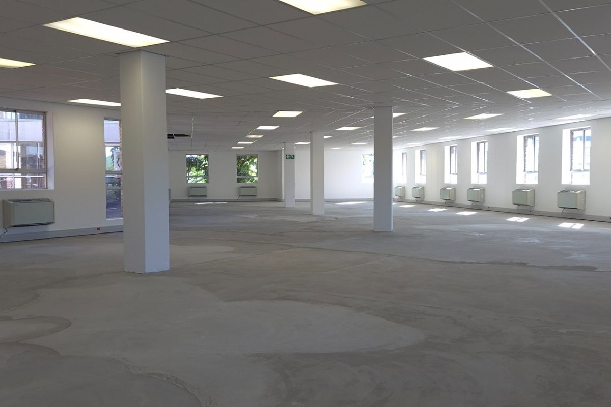 Spacious open-plan retail or office area featuring a suspended ceiling, recessed lighting, structural columns, and multiple wall-mounted HVAC units.