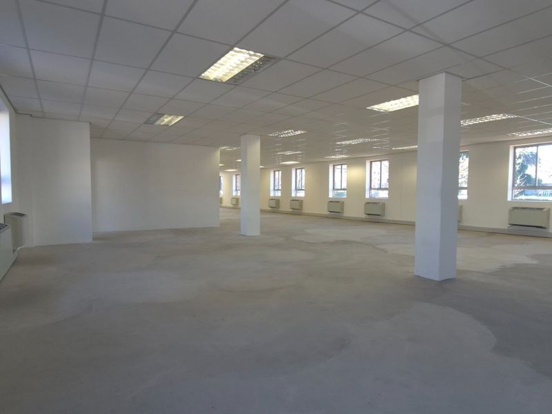 Spacious open-plan commercial interior featuring a suspended ceiling, recessed lighting, wall-mounted HVAC units, and an unfinished concrete floor.