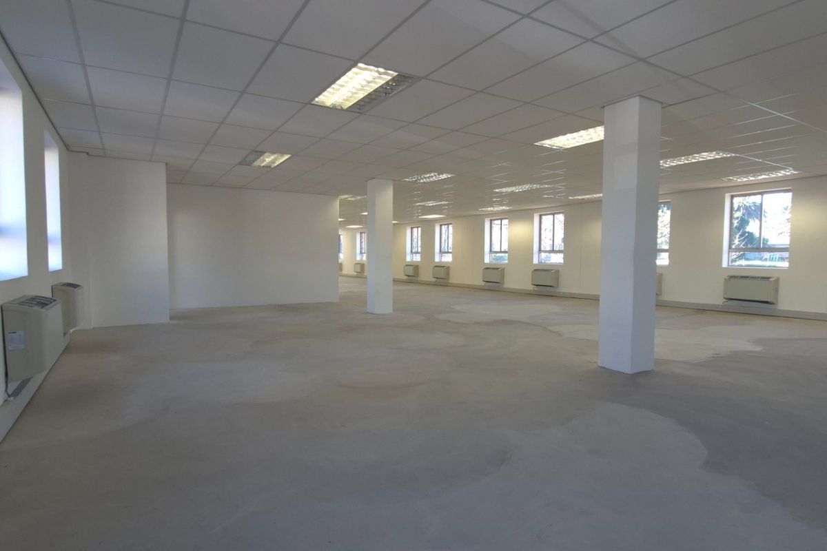 Spacious open-plan commercial interior featuring a suspended ceiling, recessed lighting, wall-mounted HVAC units, and an unfinished concrete floor.