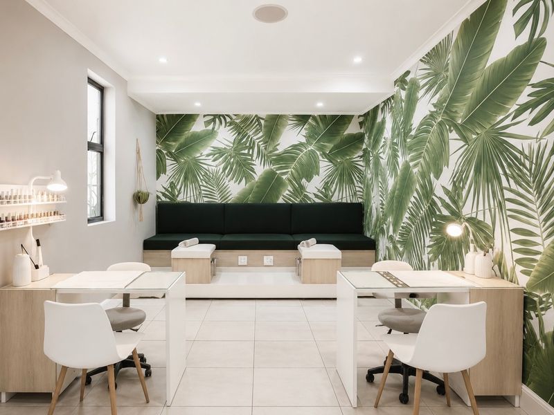 A well-maintained commercial salon space featuring built-in pedicure stations, nail technician desks, tiled flooring, and decorative palm leaf wallpaper.
