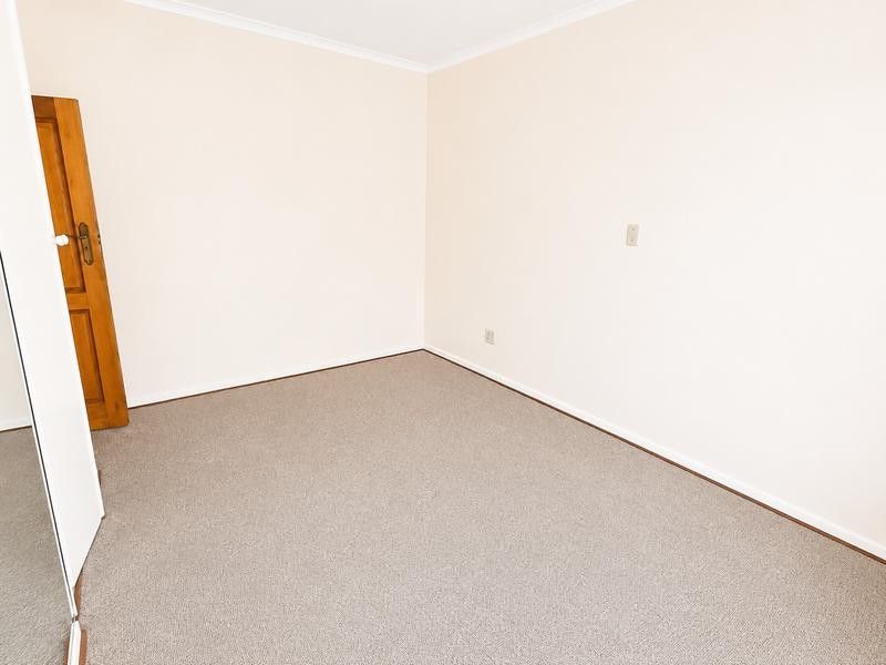 A clean, empty bedroom featuring neutral walls, carpeted flooring, and a built-in cupboard, offering a blank canvas for personalization.